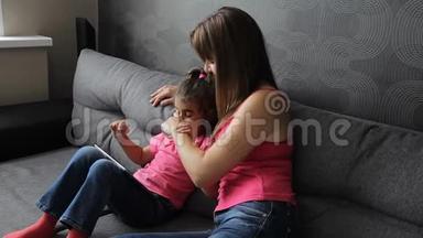 有孩子的女人用平板电脑<strong>坐在沙发</strong>上。 母亲带着孩子<strong>坐在沙发</strong>上用平板电脑